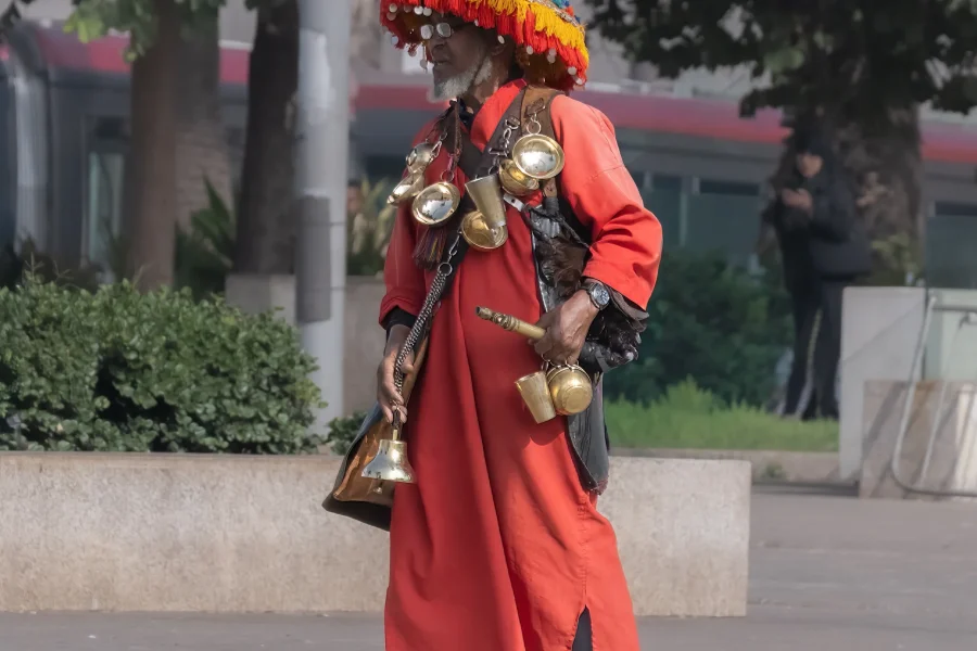 The Traditional Water Seller in Morocco: A Living Symbol of Culture and Heritage Walking through the old medinas of Morocco—especially in cities like Marrakech, Fes, Rabat, and Meknes—you may encounter a striking figure dressed in colorful traditional clothing, carrying brass cups and a decorated water container. This is the traditional Moroccan water seller, one of the most iconic symbols of Morocco’s rich cultural heritage. A Tradition Rooted in History The profession of the water seller dates back centuries, long before modern plumbing existed in Moroccan cities. At that time, access to fresh drinking water was limited, and water sellers played a vital role in daily life by providing clean water to locals, travelers, and merchants in the medina. They would collect water from natural springs, fountains, or public wells and distribute it throughout the city. Their presence ensured survival in Morocco’s warm climate and became an essential service within urban life. More Than a Job – A Cultural Identity Today, the water seller is no longer a necessity but remains a living tradition and an important part of Moroccan identity. You will often see them near busy squares, historic sites, or tourist areas, especially in Jemaa el-Fnaa Square in Marrakech, where culture, history, and daily life blend together. Their traditional outfit—often featuring a wide-brimmed hat adorned with colorful tassels—along with the sound of clinking metal cups, attracts visitors and photographers from around the world. A Symbol of Authentic Morocco For travelers seeking authentic Moroccan experiences, encountering a water seller is a reminder of Morocco’s deep respect for tradition and heritage. It reflects a time when community, simplicity, and human connection were at the heart of everyday life. Taking a photo with a water seller is not just a travel moment—it is a connection to Morocco’s past, preserved in the present. Experiencing Local Life with Moroccan Odyssey At Moroccan Odyssey, we believe true travel goes beyond monuments and landscapes. We design private and customized tours that immerse our guests in Morocco’s local traditions, daily life, and cultural stories. From walking through ancient medinas to meeting local artisans and witnessing timeless traditions like the water seller, our tours offer a deeper understanding of Morocco—guided by knowledgeable locals who share the heart of the country.