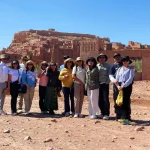 A Journey Through History, Culture, and Cinematic Landscapes Few places in Morocco capture the imagination like Ait Ben Haddou, the iconic ksar that rises from the desert plains between the High Atlas Mountains and Ouarzazate. Recognized as a UNESCO World Heritage Site, this extraordinary village of earthen clay architecture stands as one of the most complete and best-preserved examples of southern Moroccan fortified settlements. For travelers exploring Morocco with Moroccan Odyssey, visiting Ait Ben Haddou is more than a stop—it is a journey into centuries of civilization, craftsmanship, and heritage. The Story Behind a Desert Fortress Ait Ben Haddou was once an important stop on the ancient caravan route linking Marrakech to Timbuktu. Traders transporting salt, spices, gold, and other goods sought refuge inside its protective walls before continuing across the Sahara. Built entirely from earth, straw, and clay, the ksar reflects the genius of Amazigh (Berber) architecture that combines practicality, beauty, and sustainability. Its tall defensive towers, narrow alleyways, and stunning layout tell the story of a community that thrived in the harsh landscapes of southern Morocco. Each house, granary, and kasbah inside the settlement reveals the traditional lifestyle of the region. It’s a place where time seems to stand still, offering visitors a glimpse into the Morocco of centuries past. A World-Famous Filming Location Ait Ben Haddou is not only historically important—it is also one of the most filmed locations in Morocco. Its dramatic backdrop and unique architecture have attracted major international productions, including: • Gladiator • The Mummy • Lawrence of Arabia • Prince of Persia • Game of Thrones (the city of Yunkai) These appearances have added to its global fame, making it a must-see for cinema lovers, photographers, and cultural travelers alike. Your Experience with Moroccan Odyssey At Moroccan Odyssey, we include Ait Ben Haddou as a highlight on many of our private tours from Marrakech to the Sahara Desert. Our guests enjoy a fully immersive experience: • Crossing the scenic High Atlas Mountains • Visiting traditional Berber villages • Walking through the narrow alleys of the ksar • Learning about its architecture and historical importance • Climbing to the hilltop granary for panoramic desert views Our guides share stories about the families who lived here, the ancient trade routes, and the films that brought the kasbah international fame. Whether you’re traveling as a family, a couple, or a private group, Ait Ben Haddou offers a perfect blend of history, adventure, and photography. Group Visit – Picture Description (SEO-Friendly) The picture shows our group of travelers standing proudly in front of the majestic Ait Ben Haddou Kasbah under the bright desert sun. Behind them rises the ancient adobe architecture, fortified towers, and golden hillside village that symbolize Morocco’s rich cultural heritage. This photo captures a joyful moment during their private tour with Moroccan Odyssey, where they explored this world-famous UNESCO site, enjoyed the peaceful desert atmosphere, and experienced the true spirit of Moroccan hospitality and adventure. Why Ait Ben Haddou Is a Must-Visit Ait Ben Haddou is more than a historical site—it is a living landmark that offers: • Authentic cultural immersion • Spectacular desert landscapes • Traditional Berber architecture • Cinematic viewpoints perfect for photography • A deep connection to Morocco’s ancient past For travelers seeking an authentic and meaningful journey, this ksar is one of the most unforgettable places in Morocco. Plan Your Visit with Moroccan Odyssey Moroccan Odyssey specializes in custom-designed itineraries, private tours, luxury experiences, and cultural adventures across the Kingdom. Ait Ben Haddou is featured in our most popular routes, including: • Marrakech to Sahara Desert (via High Atlas & Ouarzazate) • Southern Morocco circuits • Imperial Cities & Desert extensions • Private luxury tours Our mission is to create a memorable, authentic, and well-organized journey for every guest.