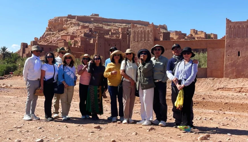 A Journey Through History, Culture, and Cinematic Landscapes Few places in Morocco capture the imagination like Ait Ben Haddou, the iconic ksar that rises from the desert plains between the High Atlas Mountains and Ouarzazate. Recognized as a UNESCO World Heritage Site, this extraordinary village of earthen clay architecture stands as one of the most complete and best-preserved examples of southern Moroccan fortified settlements. For travelers exploring Morocco with Moroccan Odyssey, visiting Ait Ben Haddou is more than a stop—it is a journey into centuries of civilization, craftsmanship, and heritage. The Story Behind a Desert Fortress Ait Ben Haddou was once an important stop on the ancient caravan route linking Marrakech to Timbuktu. Traders transporting salt, spices, gold, and other goods sought refuge inside its protective walls before continuing across the Sahara. Built entirely from earth, straw, and clay, the ksar reflects the genius of Amazigh (Berber) architecture that combines practicality, beauty, and sustainability. Its tall defensive towers, narrow alleyways, and stunning layout tell the story of a community that thrived in the harsh landscapes of southern Morocco. Each house, granary, and kasbah inside the settlement reveals the traditional lifestyle of the region. It’s a place where time seems to stand still, offering visitors a glimpse into the Morocco of centuries past. A World-Famous Filming Location Ait Ben Haddou is not only historically important—it is also one of the most filmed locations in Morocco. Its dramatic backdrop and unique architecture have attracted major international productions, including: • Gladiator • The Mummy • Lawrence of Arabia • Prince of Persia • Game of Thrones (the city of Yunkai) These appearances have added to its global fame, making it a must-see for cinema lovers, photographers, and cultural travelers alike. Your Experience with Moroccan Odyssey At Moroccan Odyssey, we include Ait Ben Haddou as a highlight on many of our private tours from Marrakech to the Sahara Desert. Our guests enjoy a fully immersive experience: • Crossing the scenic High Atlas Mountains • Visiting traditional Berber villages • Walking through the narrow alleys of the ksar • Learning about its architecture and historical importance • Climbing to the hilltop granary for panoramic desert views Our guides share stories about the families who lived here, the ancient trade routes, and the films that brought the kasbah international fame. Whether you’re traveling as a family, a couple, or a private group, Ait Ben Haddou offers a perfect blend of history, adventure, and photography. Group Visit – Picture Description (SEO-Friendly) The picture shows our group of travelers standing proudly in front of the majestic Ait Ben Haddou Kasbah under the bright desert sun. Behind them rises the ancient adobe architecture, fortified towers, and golden hillside village that symbolize Morocco’s rich cultural heritage. This photo captures a joyful moment during their private tour with Moroccan Odyssey, where they explored this world-famous UNESCO site, enjoyed the peaceful desert atmosphere, and experienced the true spirit of Moroccan hospitality and adventure. Why Ait Ben Haddou Is a Must-Visit Ait Ben Haddou is more than a historical site—it is a living landmark that offers: • Authentic cultural immersion • Spectacular desert landscapes • Traditional Berber architecture • Cinematic viewpoints perfect for photography • A deep connection to Morocco’s ancient past For travelers seeking an authentic and meaningful journey, this ksar is one of the most unforgettable places in Morocco. Plan Your Visit with Moroccan Odyssey Moroccan Odyssey specializes in custom-designed itineraries, private tours, luxury experiences, and cultural adventures across the Kingdom. Ait Ben Haddou is featured in our most popular routes, including: • Marrakech to Sahara Desert (via High Atlas & Ouarzazate) • Southern Morocco circuits • Imperial Cities & Desert extensions • Private luxury tours Our mission is to create a memorable, authentic, and well-organized journey for every guest.