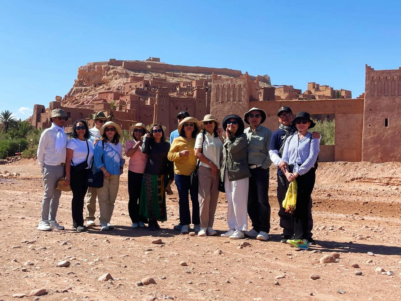 A Journey Through History, Culture, and Cinematic Landscapes Few places in Morocco capture the imagination like Ait Ben Haddou, the iconic ksar that rises from the desert plains between the High Atlas Mountains and Ouarzazate. Recognized as a UNESCO World Heritage Site, this extraordinary village of earthen clay architecture stands as one of the most complete and best-preserved examples of southern Moroccan fortified settlements. For travelers exploring Morocco with Moroccan Odyssey, visiting Ait Ben Haddou is more than a stop—it is a journey into centuries of civilization, craftsmanship, and heritage. The Story Behind a Desert Fortress Ait Ben Haddou was once an important stop on the ancient caravan route linking Marrakech to Timbuktu. Traders transporting salt, spices, gold, and other goods sought refuge inside its protective walls before continuing across the Sahara. Built entirely from earth, straw, and clay, the ksar reflects the genius of Amazigh (Berber) architecture that combines practicality, beauty, and sustainability. Its tall defensive towers, narrow alleyways, and stunning layout tell the story of a community that thrived in the harsh landscapes of southern Morocco. Each house, granary, and kasbah inside the settlement reveals the traditional lifestyle of the region. It’s a place where time seems to stand still, offering visitors a glimpse into the Morocco of centuries past. A World-Famous Filming Location Ait Ben Haddou is not only historically important—it is also one of the most filmed locations in Morocco. Its dramatic backdrop and unique architecture have attracted major international productions, including: • Gladiator • The Mummy • Lawrence of Arabia • Prince of Persia • Game of Thrones (the city of Yunkai) These appearances have added to its global fame, making it a must-see for cinema lovers, photographers, and cultural travelers alike. Your Experience with Moroccan Odyssey At Moroccan Odyssey, we include Ait Ben Haddou as a highlight on many of our private tours from Marrakech to the Sahara Desert. Our guests enjoy a fully immersive experience: • Crossing the scenic High Atlas Mountains • Visiting traditional Berber villages • Walking through the narrow alleys of the ksar • Learning about its architecture and historical importance • Climbing to the hilltop granary for panoramic desert views Our guides share stories about the families who lived here, the ancient trade routes, and the films that brought the kasbah international fame. Whether you’re traveling as a family, a couple, or a private group, Ait Ben Haddou offers a perfect blend of history, adventure, and photography. Group Visit – Picture Description (SEO-Friendly) The picture shows our group of travelers standing proudly in front of the majestic Ait Ben Haddou Kasbah under the bright desert sun. Behind them rises the ancient adobe architecture, fortified towers, and golden hillside village that symbolize Morocco’s rich cultural heritage. This photo captures a joyful moment during their private tour with Moroccan Odyssey, where they explored this world-famous UNESCO site, enjoyed the peaceful desert atmosphere, and experienced the true spirit of Moroccan hospitality and adventure. Why Ait Ben Haddou Is a Must-Visit Ait Ben Haddou is more than a historical site—it is a living landmark that offers: • Authentic cultural immersion • Spectacular desert landscapes • Traditional Berber architecture • Cinematic viewpoints perfect for photography • A deep connection to Morocco’s ancient past For travelers seeking an authentic and meaningful journey, this ksar is one of the most unforgettable places in Morocco. Plan Your Visit with Moroccan Odyssey Moroccan Odyssey specializes in custom-designed itineraries, private tours, luxury experiences, and cultural adventures across the Kingdom. Ait Ben Haddou is featured in our most popular routes, including: • Marrakech to Sahara Desert (via High Atlas & Ouarzazate) • Southern Morocco circuits • Imperial Cities & Desert extensions • Private luxury tours Our mission is to create a memorable, authentic, and well-organized journey for every guest.