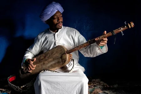 Discover Khamlia Village: Authentic Gnaoua Music and Sahara Culture Captured by Vlad and His Family During Their Moroccan Odyssey Tour Khamlia Village & the Soul of Gnaoua Music – A Cultural Journey with Moroccan Odyssey and Vlad’s Family Hidden at the edge of the golden dunes of Merzouga, Khamlia Village is one of Morocco’s most authentic cultural treasures. Known as the village of the Gnaoua, this small community preserves centuries-old spiritual music, warm hospitality, and a deep connection to Africa’s Saharan heritage. During his journey with Moroccan Odyssey, photographer Vlad from Romania, travelling with his family, captured a profound moment: a Gnaoua musician performing in the heart of Khamlia, bringing the desert’s rhythm to life. ⸻ Khamlia Village – A Gateway to Sahara Traditions Located near Merzouga and the spectacular Erg Chebbi dunes, Khamlia is a peaceful desert village famous for its vibrant musical heritage. The people of Khamlia trace their roots back to sub-Saharan Africa, mainly Ghana, Sudan, and other regions of West Africa. Their ancestors arrived in Morocco centuries ago, bringing with them unique rhythms, spiritual practices, and storytelling traditions. Today, the village is known for: • Traditional Gnaoua performances • Warm community hospitality • Cultural gatherings and music ceremonies • Its connection to desert nomadism and Saharan heritage Travelers visiting Khamlia often describe it as a place where you can feel the heartbeat of the Sahara. ⸻ The Legacy of Gnaoua Music Gnaoua music is more than entertainment—it is a spiritual art form. The musicians use: • Guembri (three-string bass lute) • Qraqeb (metal castanets) • Deep chants and rhythmic beats Their performances celebrate freedom, healing, and ancestral memory. Gnaoua music has influenced Moroccan culture deeply and is now recognized worldwide, especially through festivals in Essaouira and local ceremonies across Morocco. In Khamlia, however, you experience this music in its most authentic and intimate form. ⸻ A Moment Captured – Vlad’s Experience with Moroccan Odyssey During their private desert tour with Moroccan Odyssey, Vlad and his family visited Khamlia Village. Passionate about photography, Vlad was captivated by the authenticity of the experience and the connection between the musicians and their heritage. One of his most striking photographs features a Gnaoua musician wearing traditional attire and playing the guembri—a powerful symbol of Saharan identity. The warm tones of the desert light, the serenity of the musician, and the richness of tradition come together to tell a story of culture, history, and soul. Vlad and his family enjoyed: • A warm welcome from the local community • A live Gnaoua performance • Learning about the origins of the Gnaoua people • Exploring Merzouga, Erg Chebbi, and the surrounding nomadic lifestyle • Riding camels during sunset and visiting desert camps • Experiencing Moroccan hospitality through Moroccan Odyssey’s personalized service They expressed how meaningful it was to discover not only Morocco’s landscapes but also its living culture, guided by expert local knowledge. ⸻ Moroccan Odyssey – Connecting Travelers with Authentic Morocco At Moroccan Odyssey, we believe travel should be a personal and meaningful experience. Visits like the one to Khamlia allow guests to connect with the real Morocco—its people, music, and heritage—not just its landscapes. Our private and customizable tours offer: • Cultural encounters • Desert adventures • Luxury and comfort • Professional guides with deep knowledge • Authentic experiences designed with heart Just like Vlad and his family, every guest becomes part of our story and takes home unforgettable memories of Morocco.