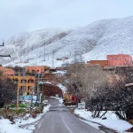 Snow-covered mountain village in Morocco with winter road and Atlas Mountains in the background