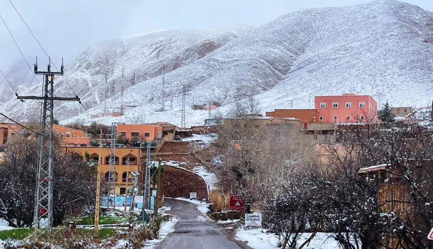 Snow-covered mountain village in Morocco with winter road and Atlas Mountains in the background