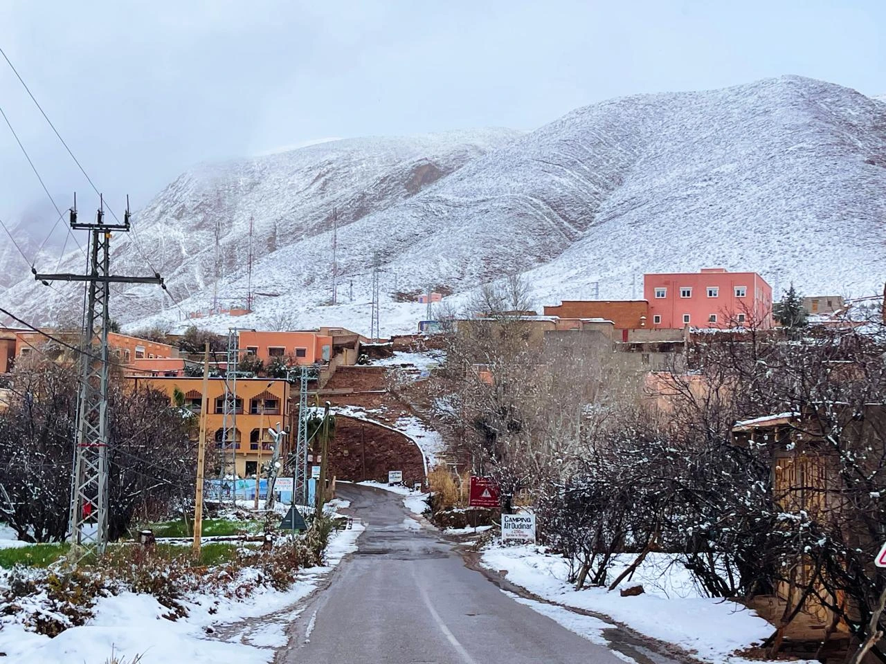 Snow-covered mountain village in Morocco with winter road and Atlas Mountains in the background