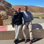 Guest and local guide enjoying a scenic stop in Dades Valley, Morocco, with stunning mountain landscapes and river views during a private desert tour