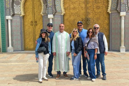 Group of travelers enjoying a private cultural tour in Fes Morocco in front of the magnificent Royal Palace gates with traditional Moroccan architecture.